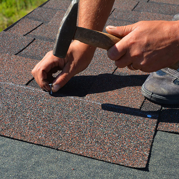 Worker hammering in asphalt shingles